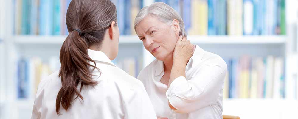 Senior woman holding her neck due to fibromyalgia pain talking to her female doctor about medical cannabis treatment options